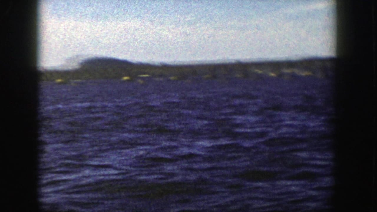 1958 Wisconsin 8mm frame showing rippled blue water, a low horizon, bright sky, and dark gate edges.
