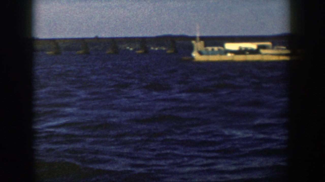 A tan barge-like vessel appears on deep blue water in 1958 Wisconsin footage, with a low structure behind it.