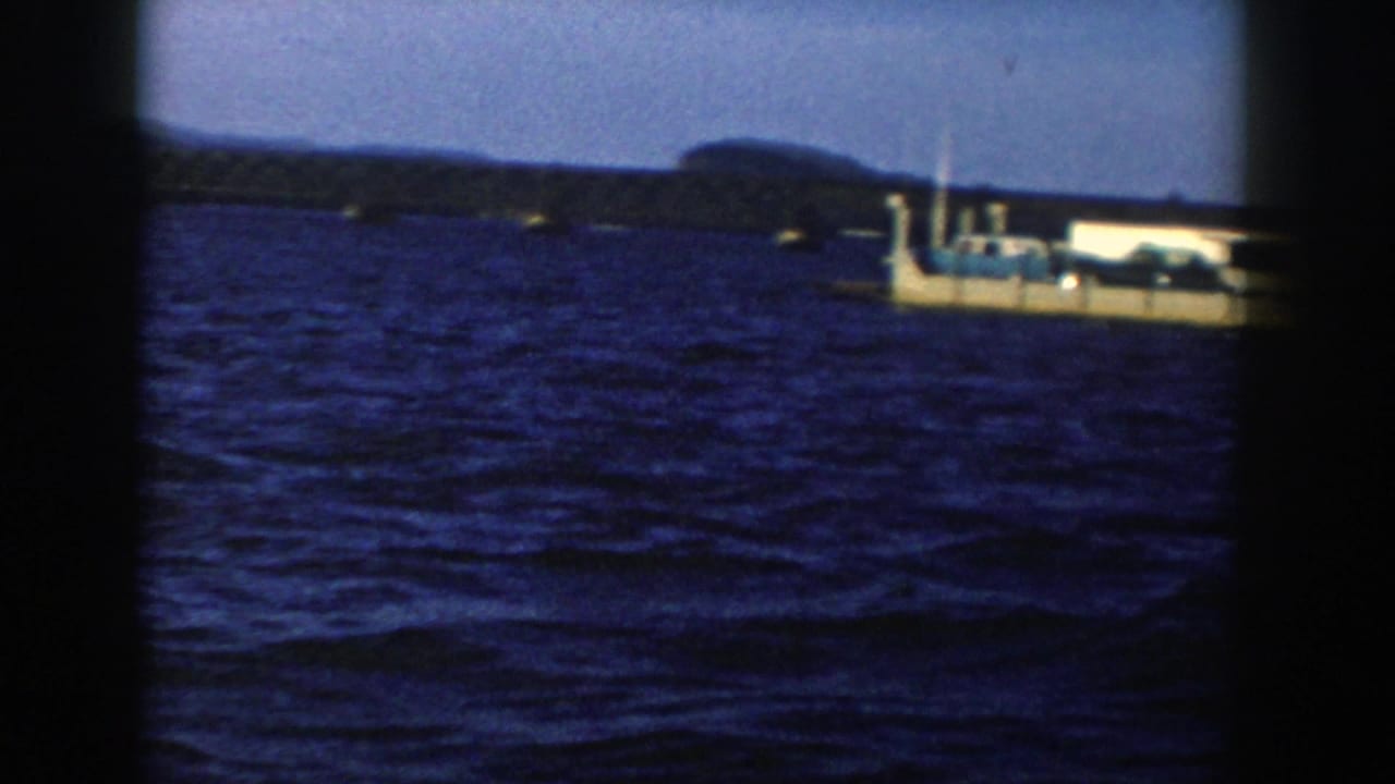 Small ferry crossing a blue lake with distant shoreline and hills.