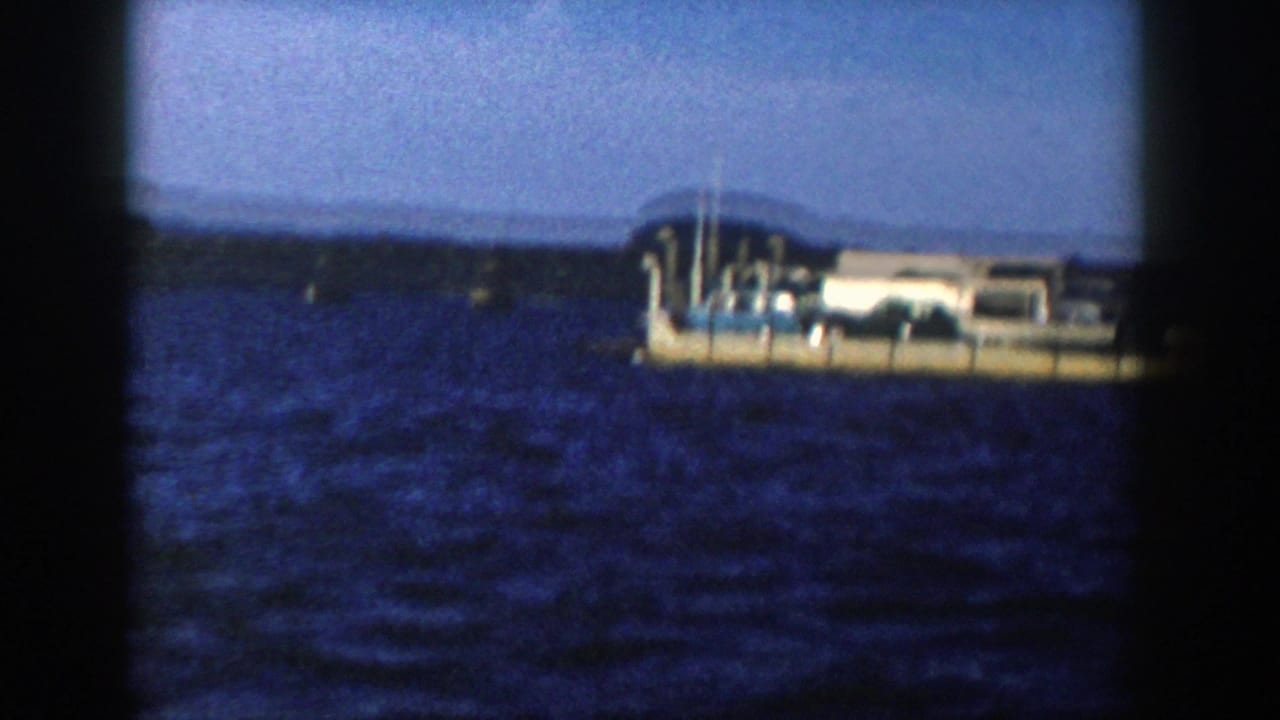 The ferry appears closer to the right edge of the 1958 Wisconsin lake scene, with rippled water and a dark shoreline in the distance.