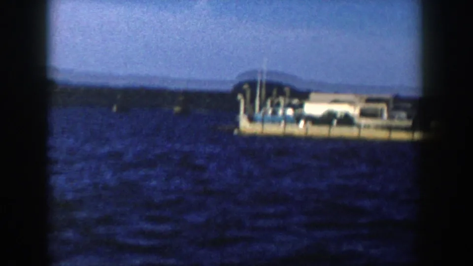 The ferry appears closer to the right edge of the 1958 Wisconsin lake scene, with rippled water and a dark shoreline in the distance.