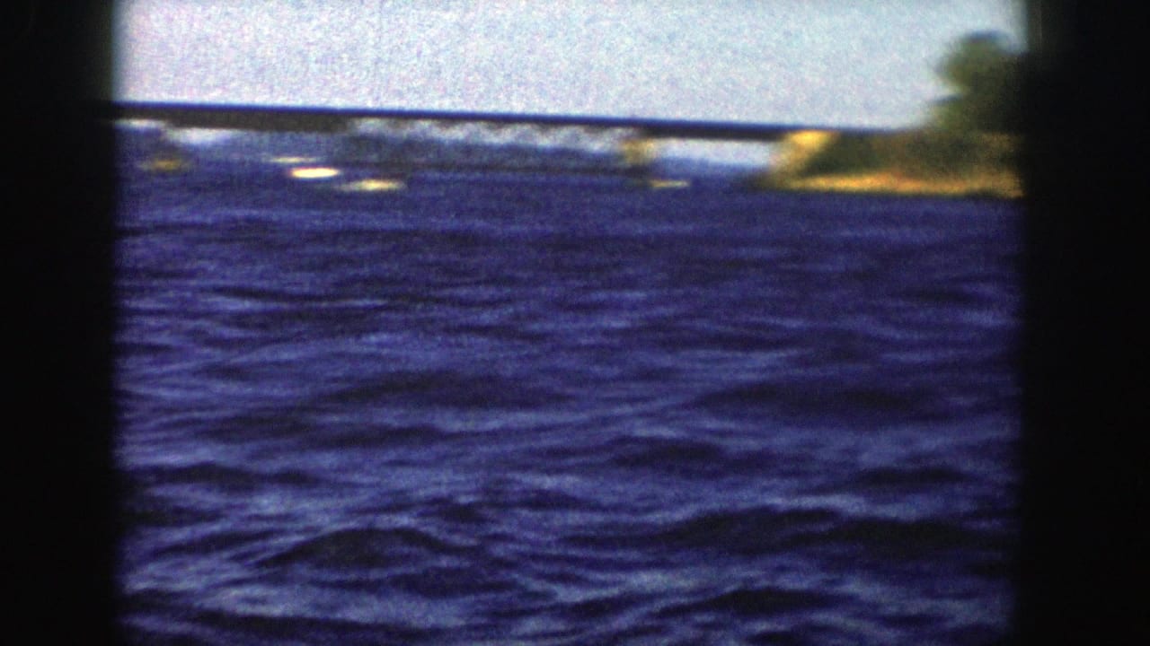 The final frame shows choppy blue lake water, a distant low bridge or causeway, and a small stretch of shoreline in 1958 Wisconsin footage.