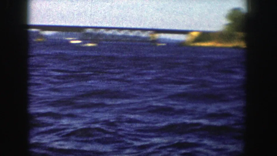 The final frame shows choppy blue lake water, a distant low bridge or causeway, and a small stretch of shoreline in 1958 Wisconsin footage.