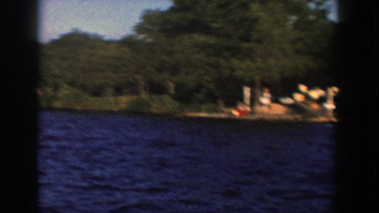 1958 Wisconsin 8mm view from a boat, with choppy blue water, dense trees, and a small dock or shore landing at right.