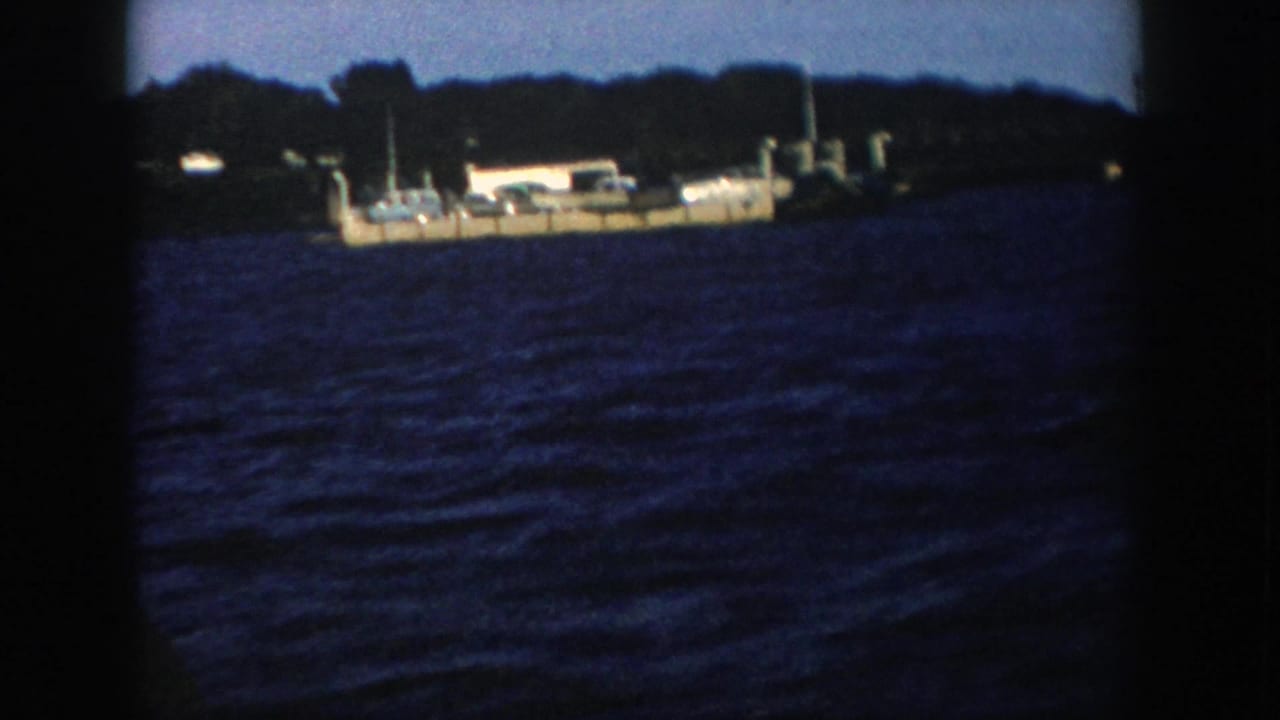 1958 Wisconsin 8mm still with a small ferry or barge moving across choppy water, seen through soft handheld framing.