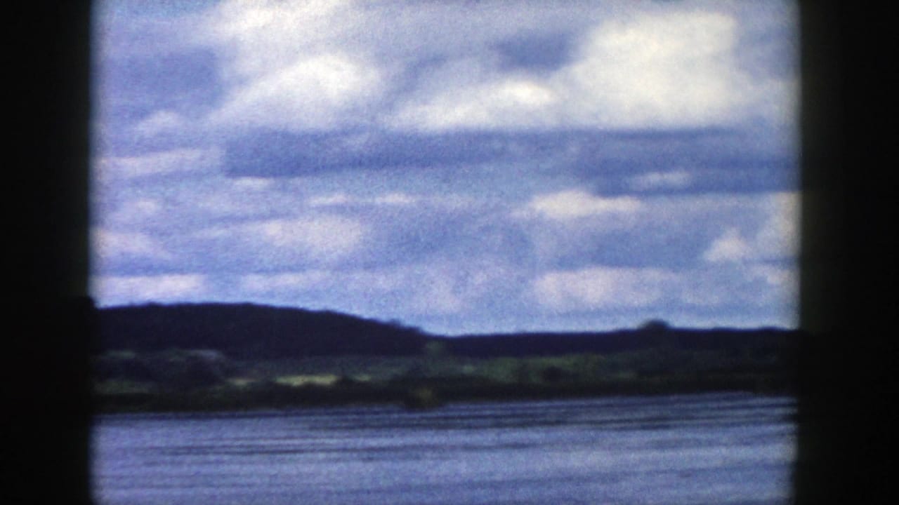1958 Wisconsin landscape view from a moving vehicle, with water in the foreground, rolling hills beyond, and dark window framing.