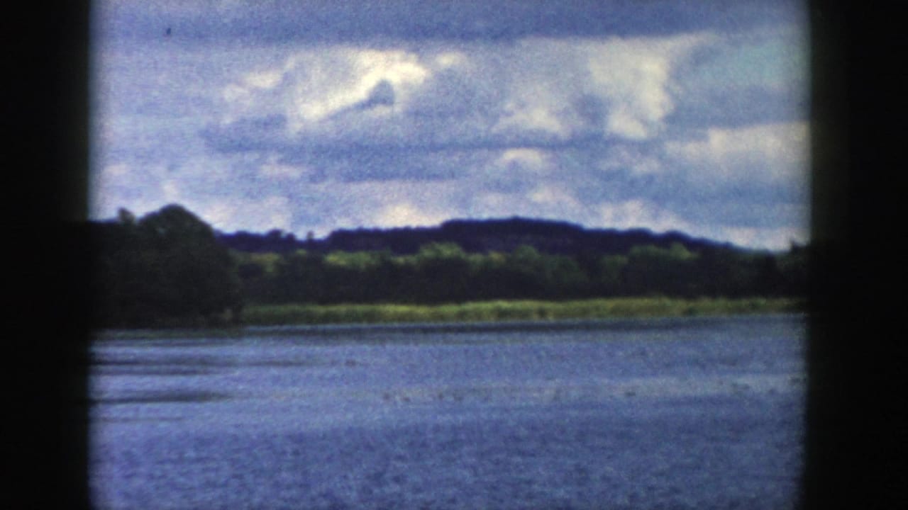 1958 Wisconsin lake view with rippled blue water, green shoreline, low hills, and bright cloud cover.