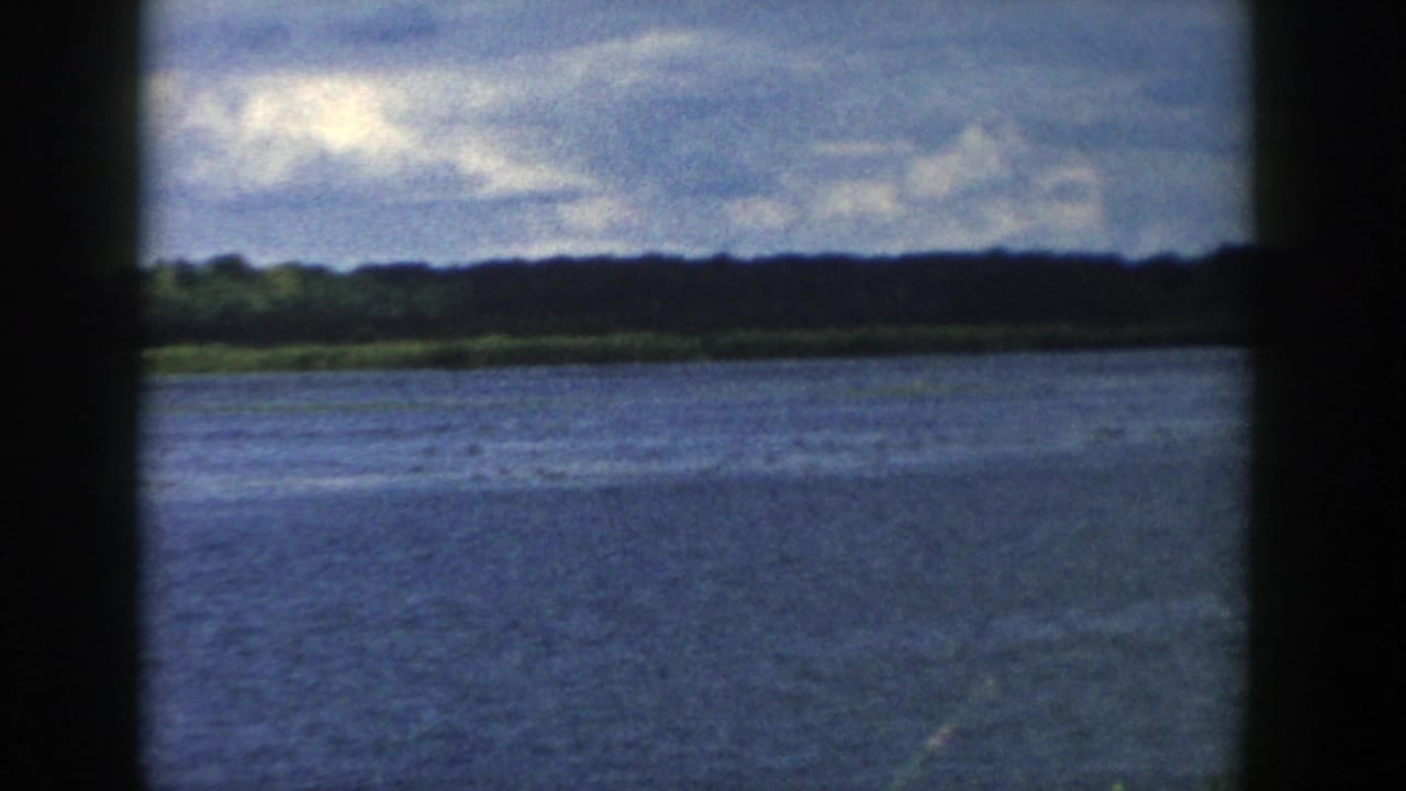 1958 Wisconsin frame showing open lake water, a dark forested horizon, and scattered clouds overhead.