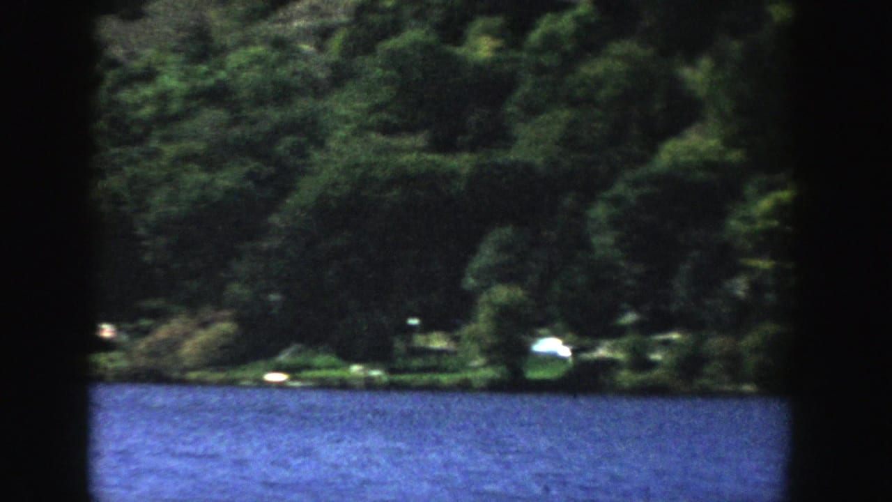 1958 Wisconsin home-movie frame showing rippled blue lake water and a dark green wooded shoreline across the water.