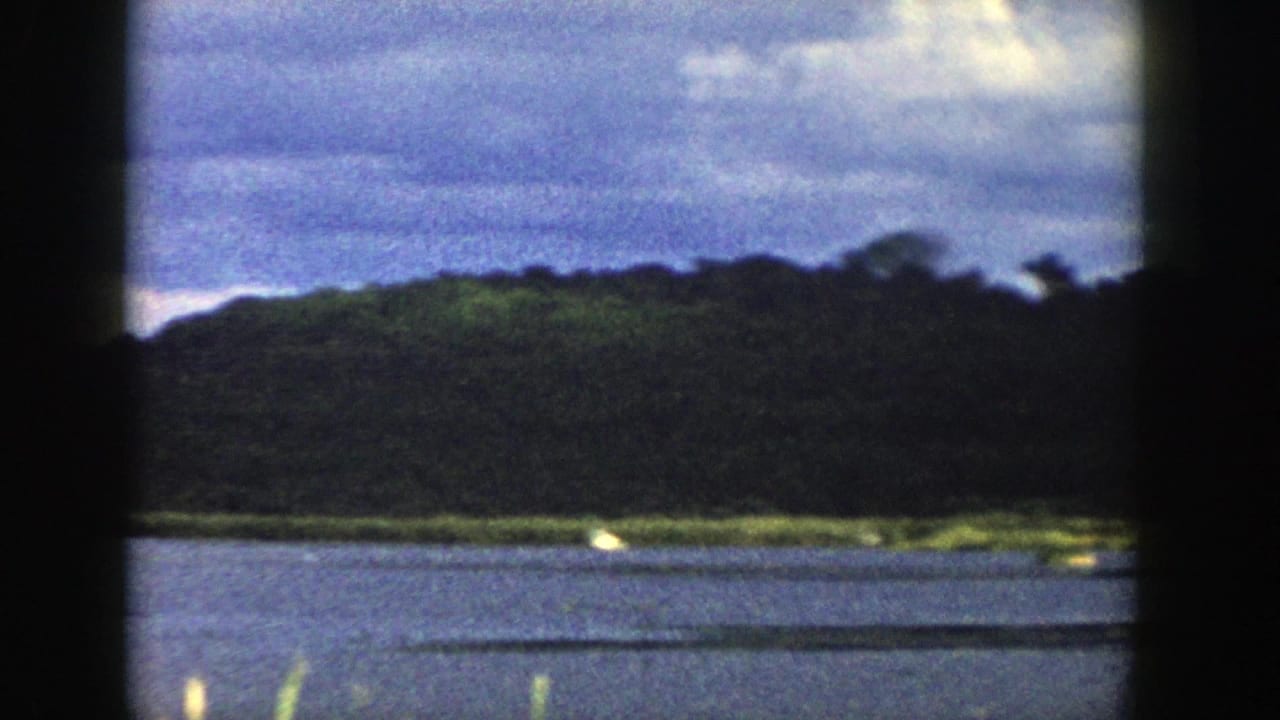 Wisconsin riverbank and wooded hills appear through the train window, with soft focus, blue water, shoreline grass, and cloudy sky.