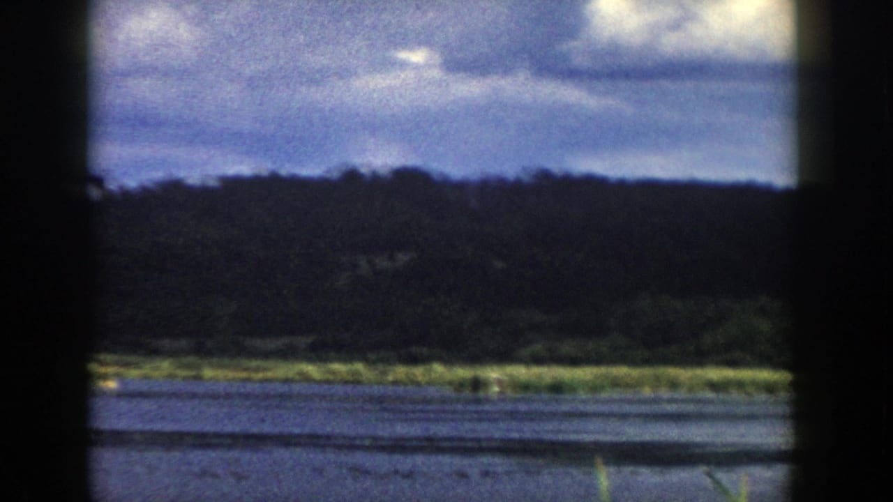 A late-frame train-window view shows the Wisconsin river, dark tree-covered hills, reflective water, and blue-gray clouds on 8mm film.