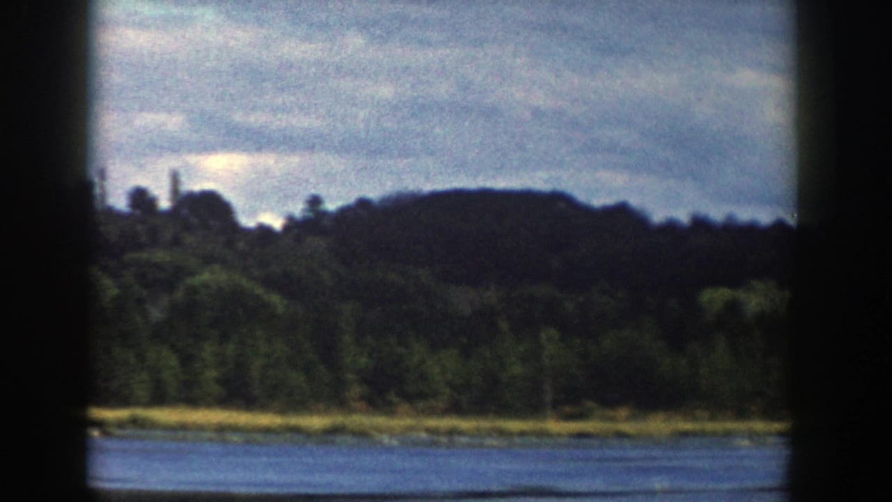 End of the 1958 Wisconsin 8mm pan, showing water, a narrow bright shoreline, dark wooded land, and layered clouds.