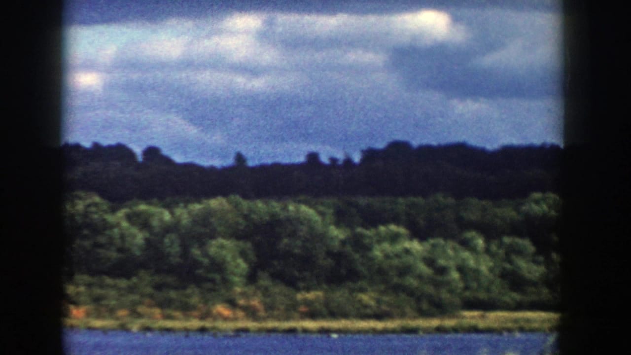1958 Wisconsin home-movie frame of a broad river and tree-covered shoreline, with heavy dark borders from the 8mm frame scan.
