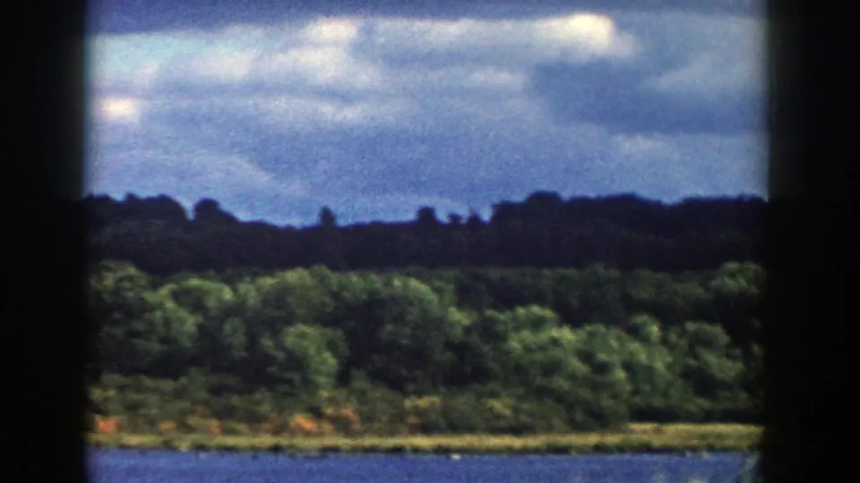 1958 Wisconsin home-movie frame of a broad river and tree-covered shoreline, with heavy dark borders from the 8mm frame scan.