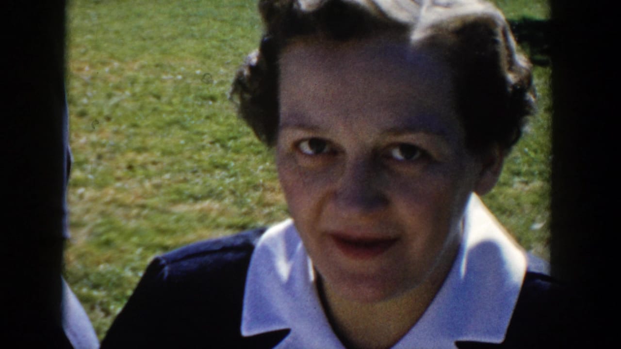 A second adult woman in dark clothing with a white collar looks toward the camera in the sunny Wisconsin yard scene.