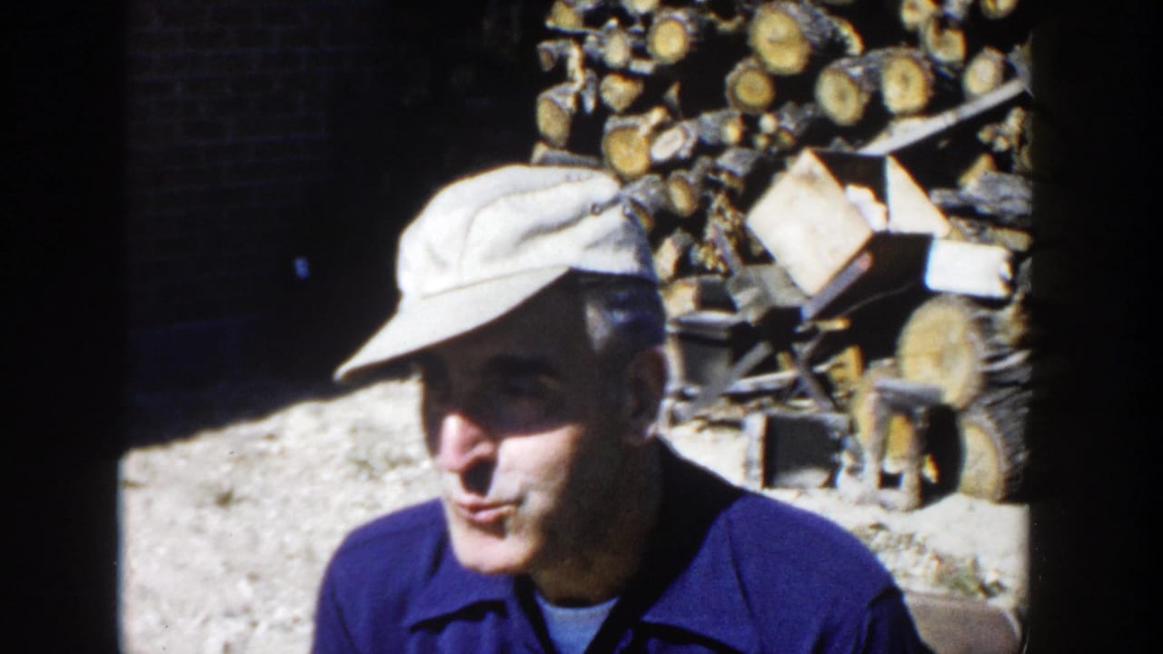 In 1958 Wisconsin home-movie footage, a man in a light cap and blue work shirt stands near a large stack of chopped firewood.