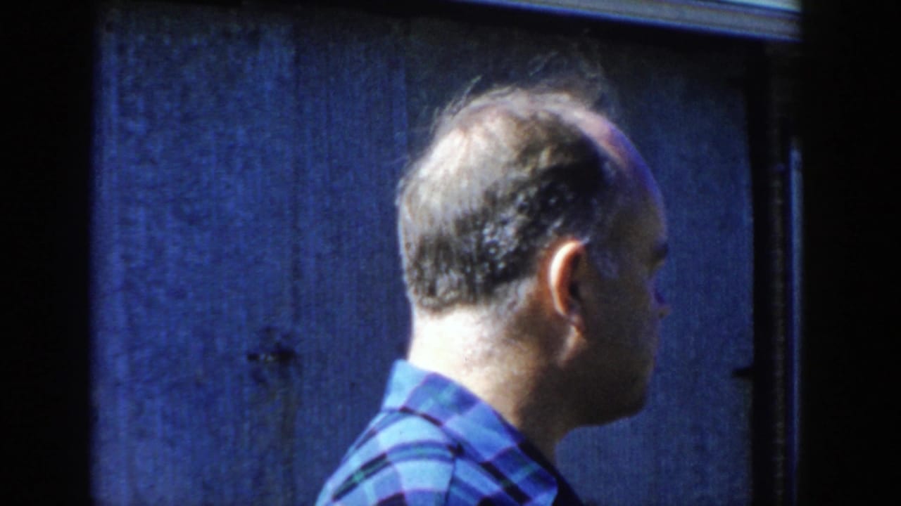 The same man appears in side profile in the 1958 Wisconsin home-movie frame, standing close to a dark blue wall.