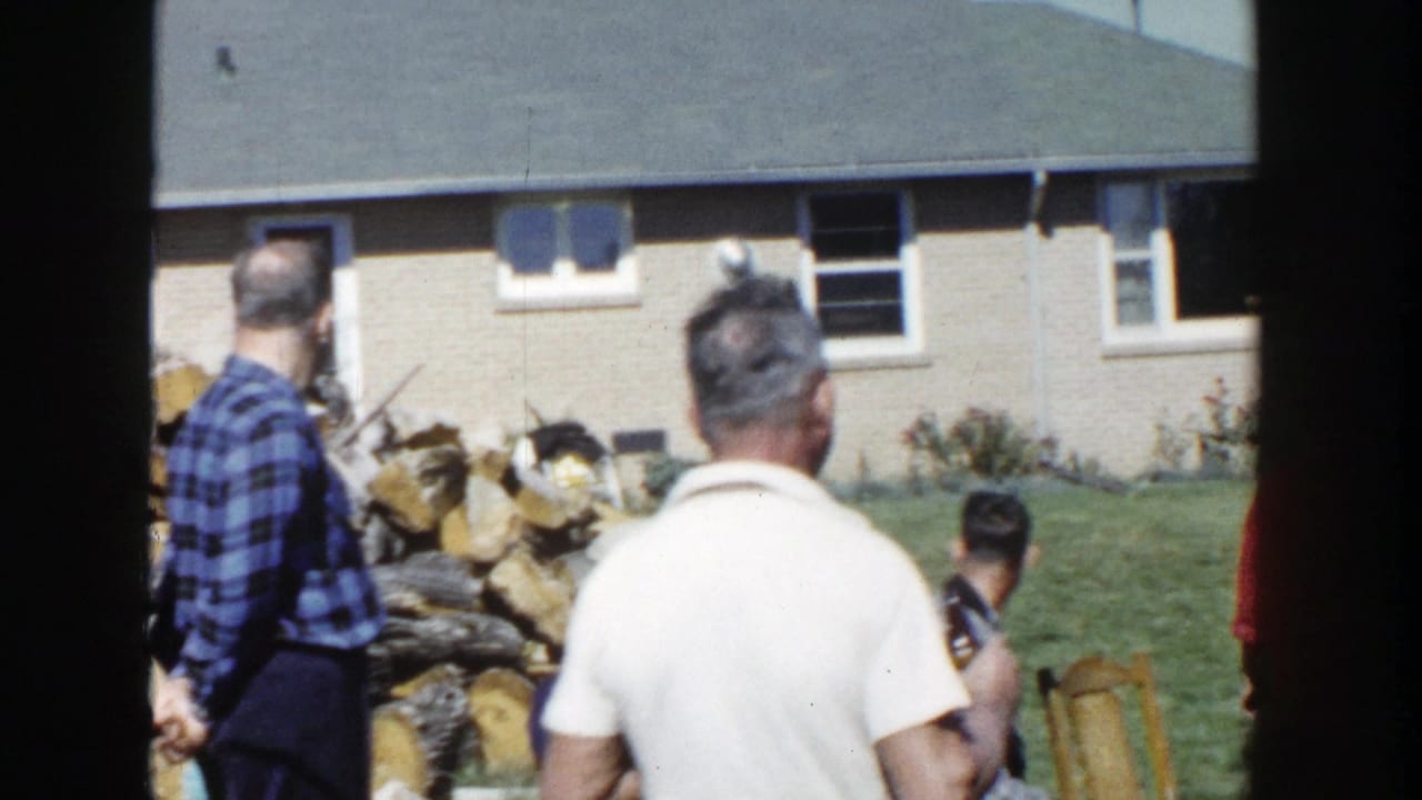 1958 Wisconsin backyard scene with men in casual shirts near a large firewood stack and brick suburban house.