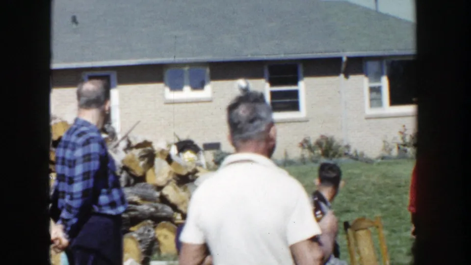 1958 Wisconsin backyard scene with men in casual shirts near a large firewood stack and brick suburban house.