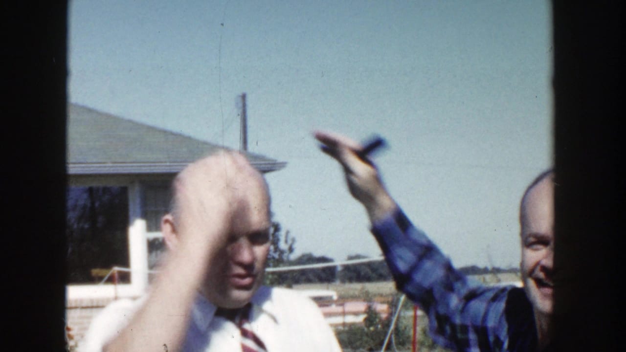 The man in the white shirt touches his head as the plaid-shirted man raises a small object during the playful exchange.