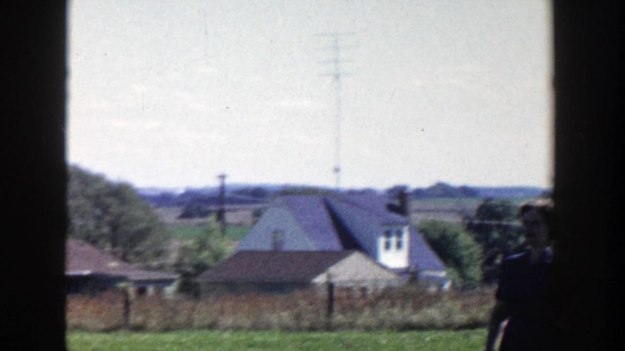 Rural houses and fields seen through a dark window frame.