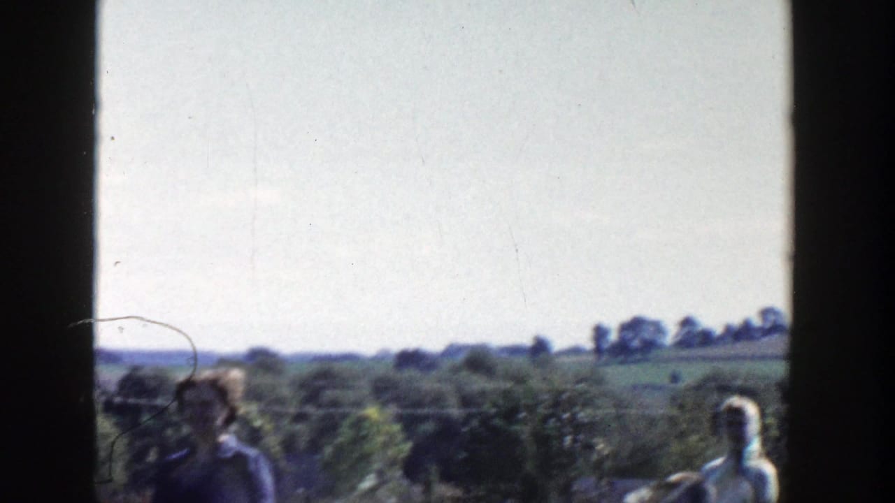 Adults appear in a rural Wisconsin yard or garden area, with trees, fields, and distant houses beyond the frame.