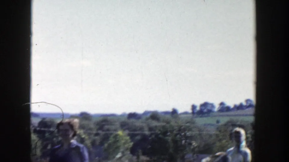 Adults appear in a rural Wisconsin yard or garden area, with trees, fields, and distant houses beyond the frame.