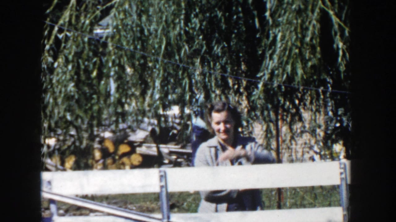 A man stands behind a white fence under a weeping willow in the 1958 Wisconsin home-movie scene.