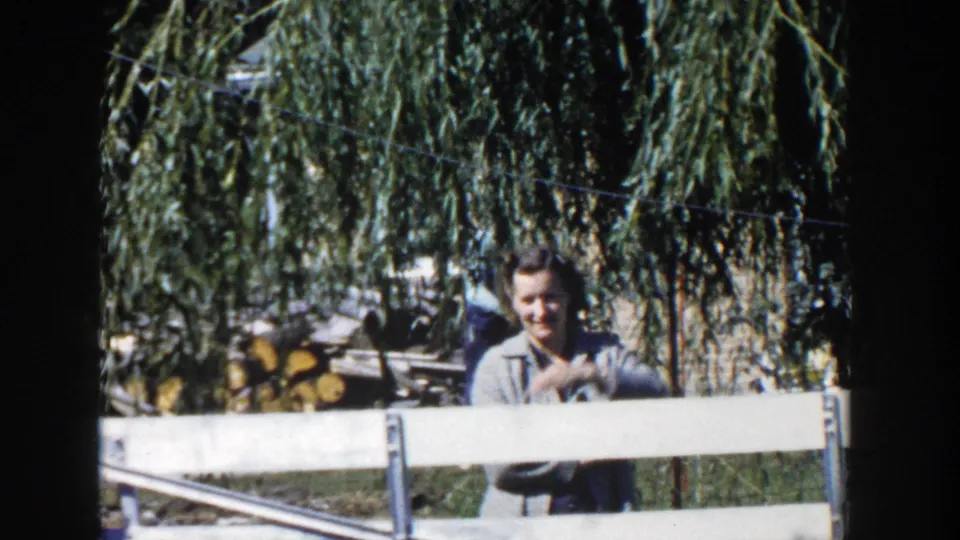A man stands behind a white fence under a weeping willow in the 1958 Wisconsin home-movie scene.