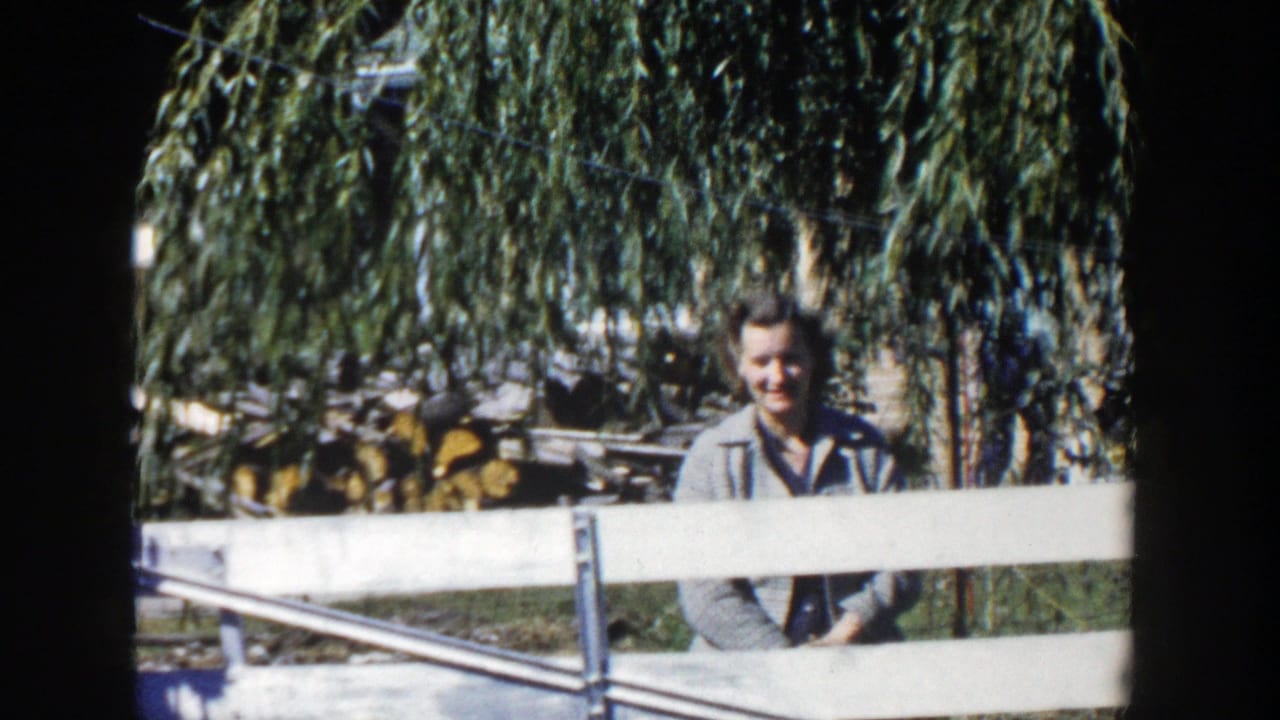 The woman remains behind the fence in the Wisconsin backyard, smiling toward the home-movie camera beneath hanging willow branches.