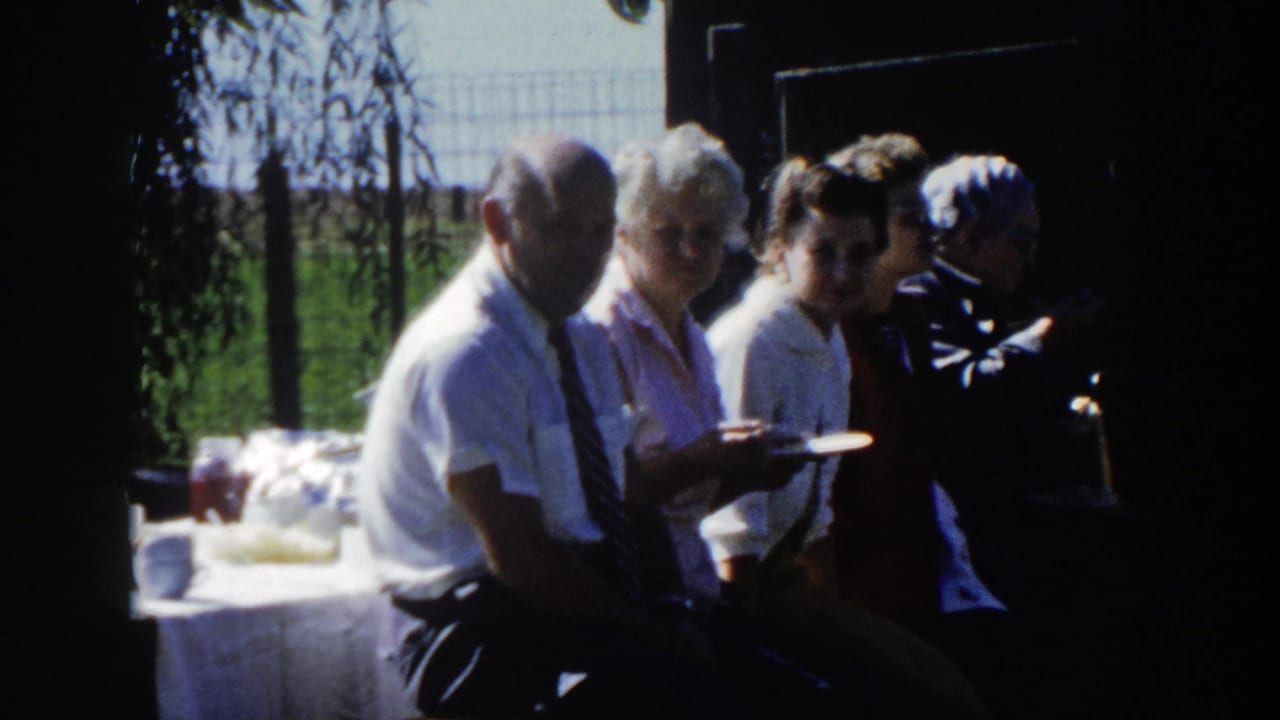 Several adults sit close together near an outdoor table in the same home-movie clip, suggesting a family gathering or picnic in Wisconsin.