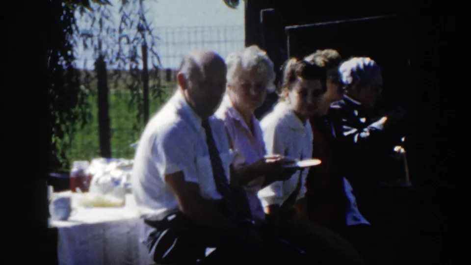 Several adults sit close together near an outdoor table in the same home-movie clip, suggesting a family gathering or picnic in Wisconsin.