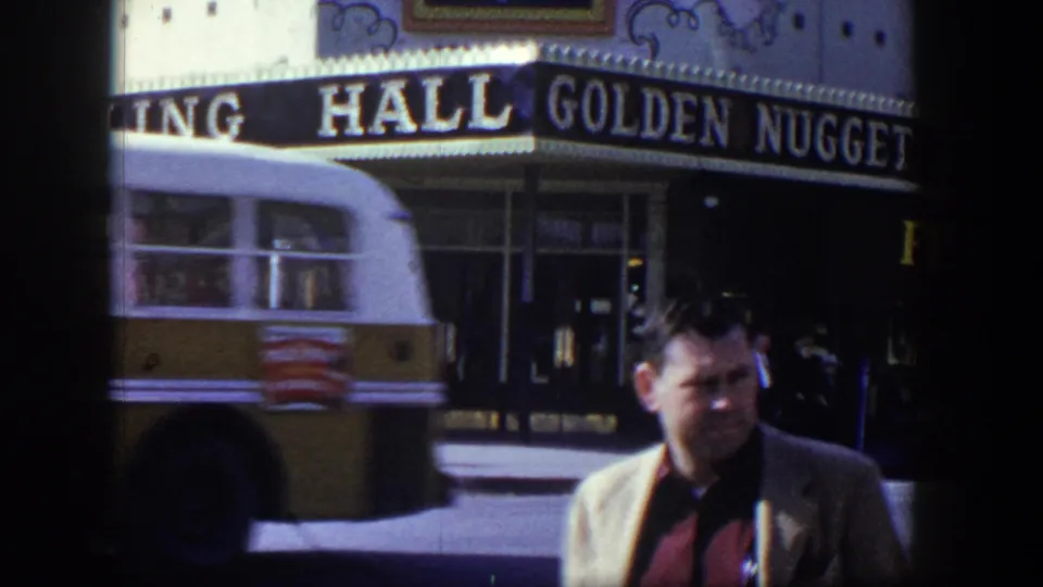 1954 Las Vegas street view of the Golden Nugget Gambling Hall, partly obscured by a passing vehicle and foreground man.
