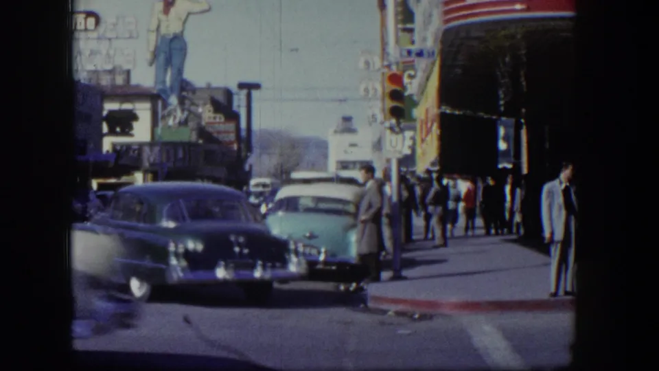 1954 Las Vegas street view with parked and moving cars, pedestrians, traffic signals, and visible casino-area signage.