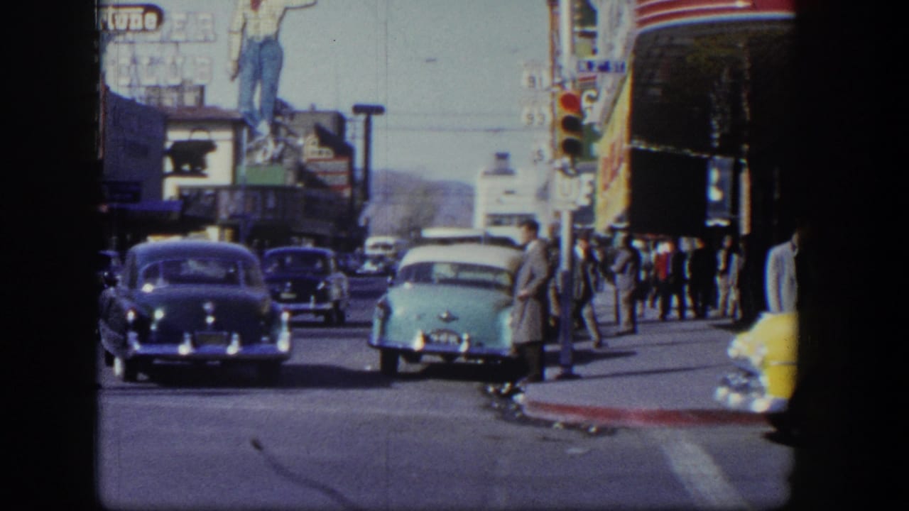Curbside Las Vegas street view with classic cars, pedestrians, traffic lights, and neon signage.