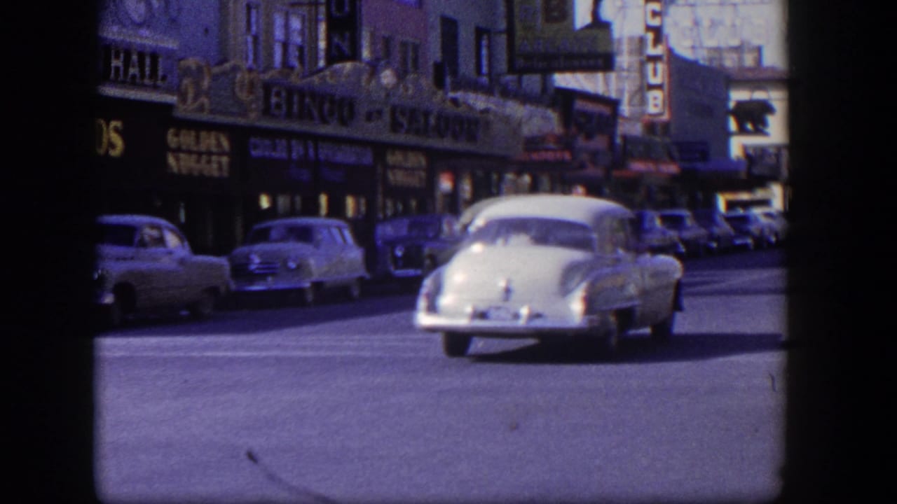 White mid-century sedan driving past gambling hall and bingo saloon storefronts.