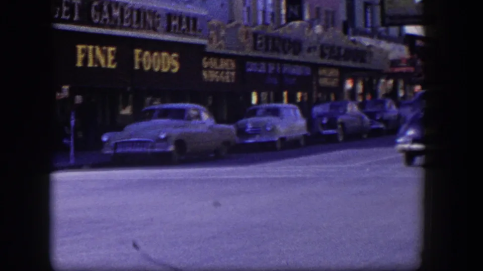 Las Vegas storefront row with parked 1950s cars beneath fine foods, market, gambling hall, and bingo saloon signs.