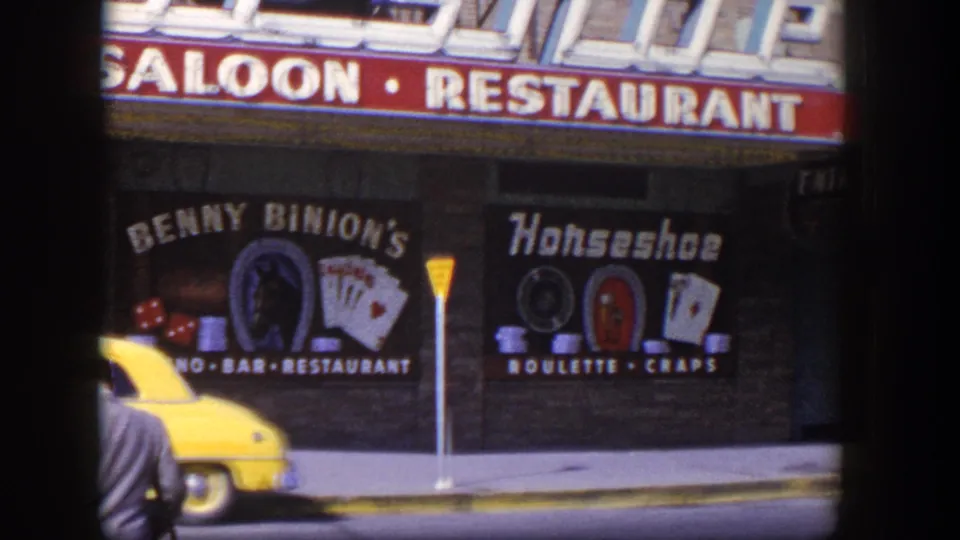 1954 Las Vegas frame with a yellow taxi near Benny Binion's Horseshoe casino signage and a sidewalk signpost.