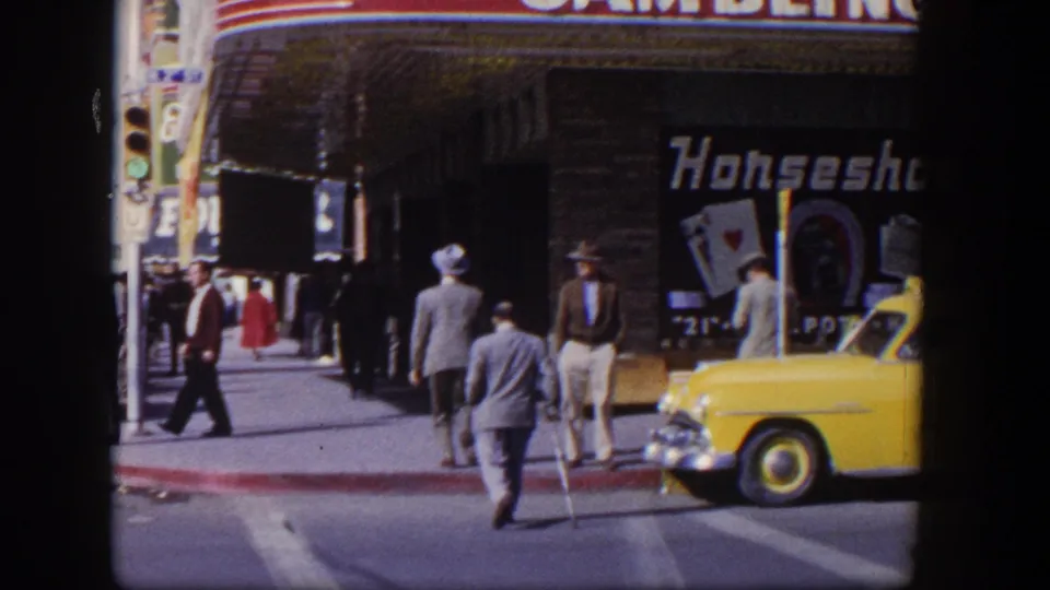 1954 Las Vegas street view showing men crossing near the Horseshoe storefront as a yellow taxi remains at the curb.