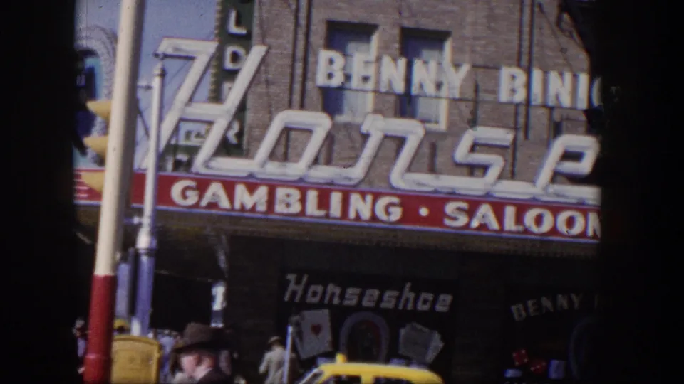 1954 Las Vegas storefront view with large gambling and saloon signage, pedestrians below, and part of a yellow car.