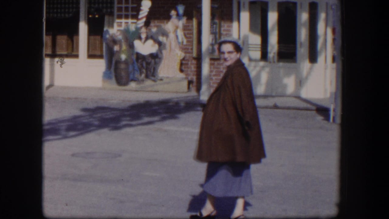 Woman in a brown coat walks on a sidewalk past a storefront display.