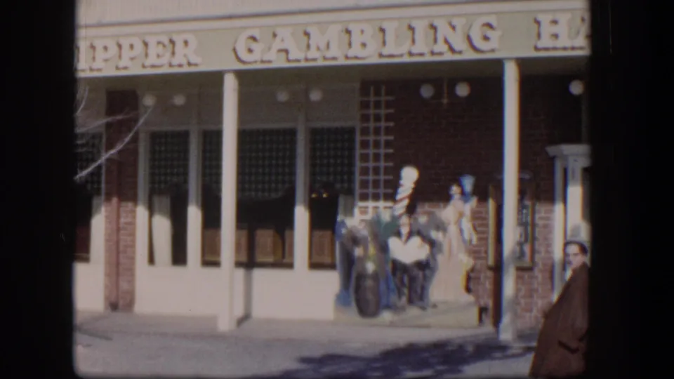 1954 Las Vegas storefront view with the Clipper Gambling Hall sign, display figures, and a person in a red coat at the right edge.