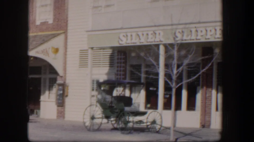 1954 Las Vegas home-movie frame with the Silver Slipper facade, green carriage, bare tree, and partial adjacent doorway.