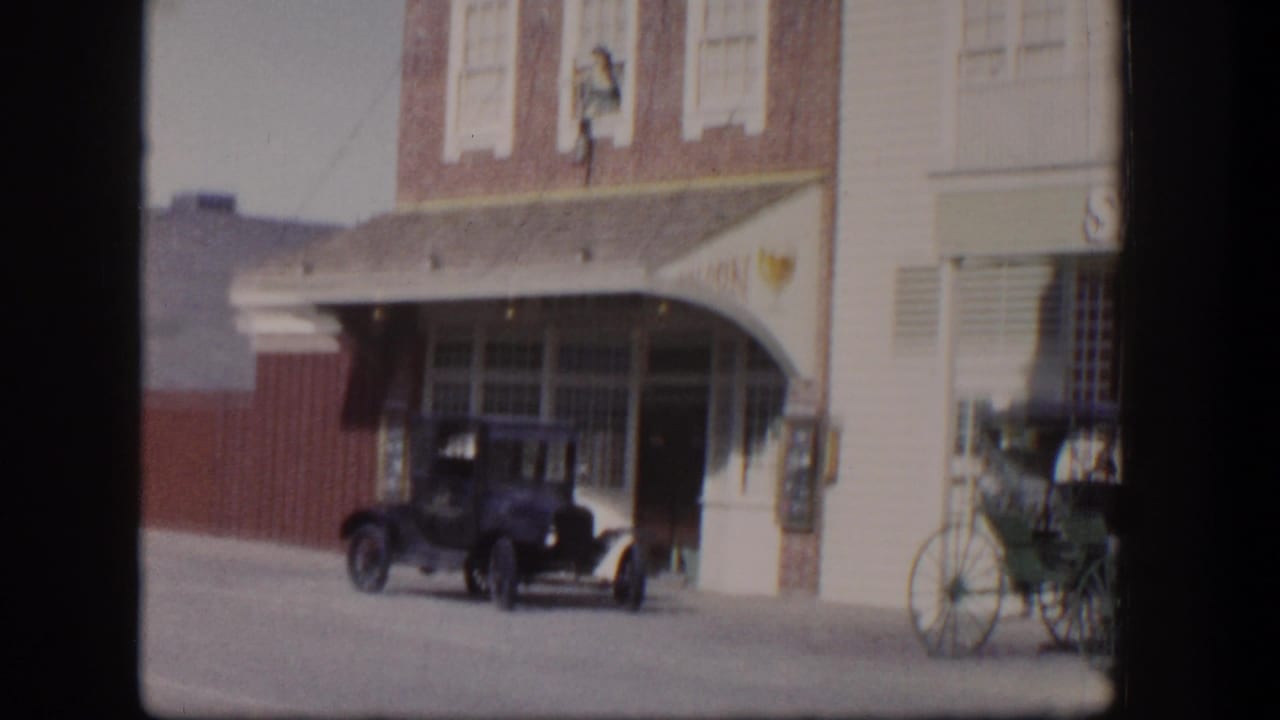 Street storefront with early car and horse-drawn carriage visible near an awning.