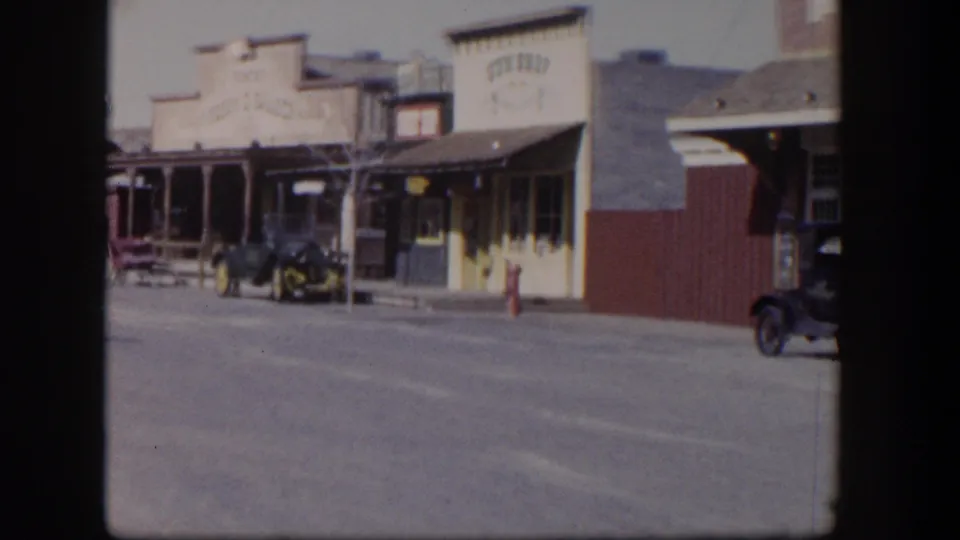 1954 Las Vegas street view with western-style storefronts, painted signage, parked early automobiles, and a red hydrant.
