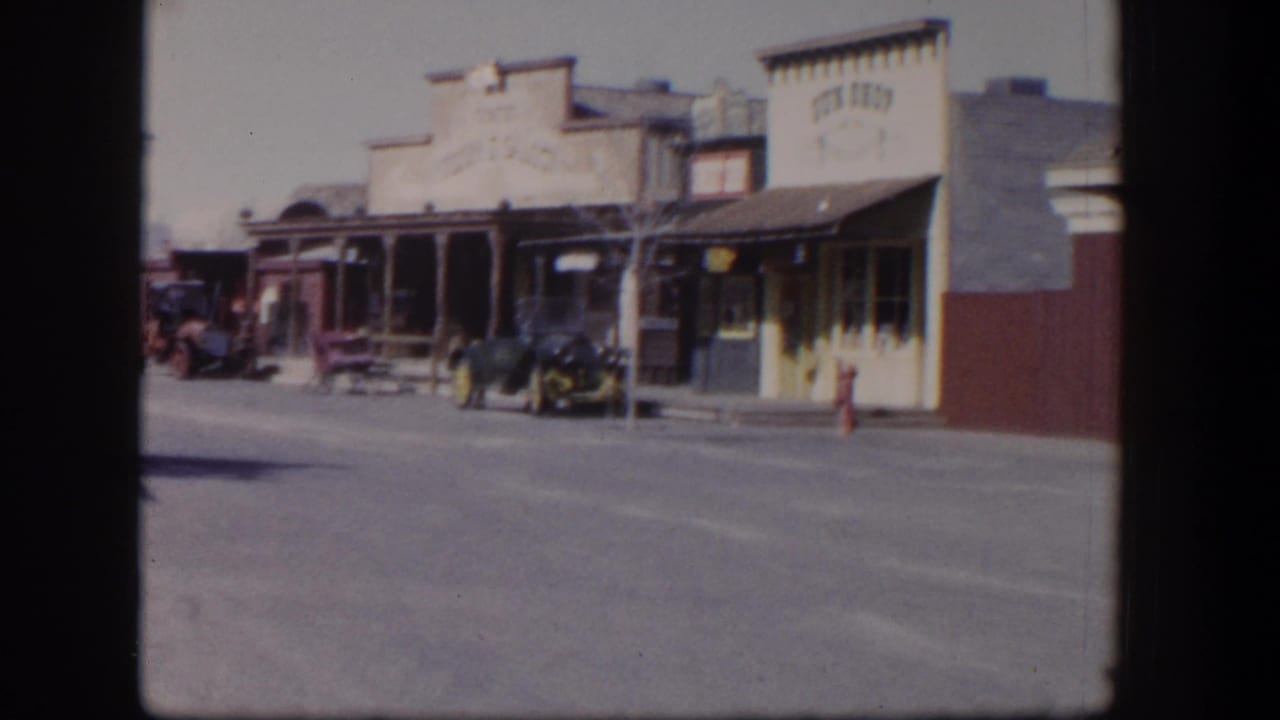 Quiet street with older storefronts and parked period cars.