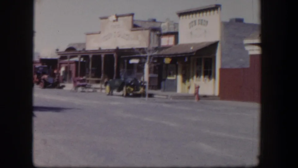 1954 Las Vegas street view with older storefront facades, parked cars, a broad roadway, and soft 8mm color.