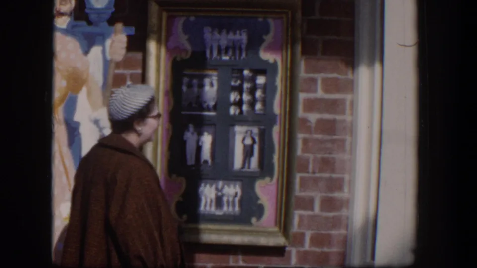 A woman in 1954 Las Vegas stands beside a brick storefront, looking at a framed display of black-and-white photographs.