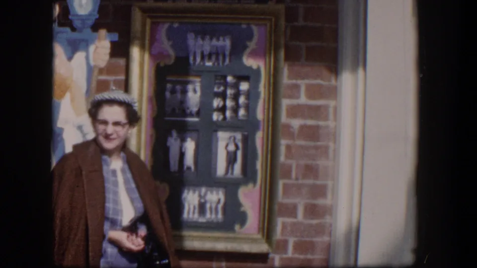 A woman in a brown coat and patterned dress faces the camera beside a storefront photo display in Las Vegas, Nevada.