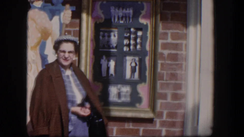 A smiling woman stands by a framed black-and-white photo display on a brick storefront wall in the 1954 Las Vegas clip.
